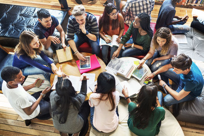 Photographie d'étudiants et d'étudiantes assis discutant en équipe avec des livres ouverts.
